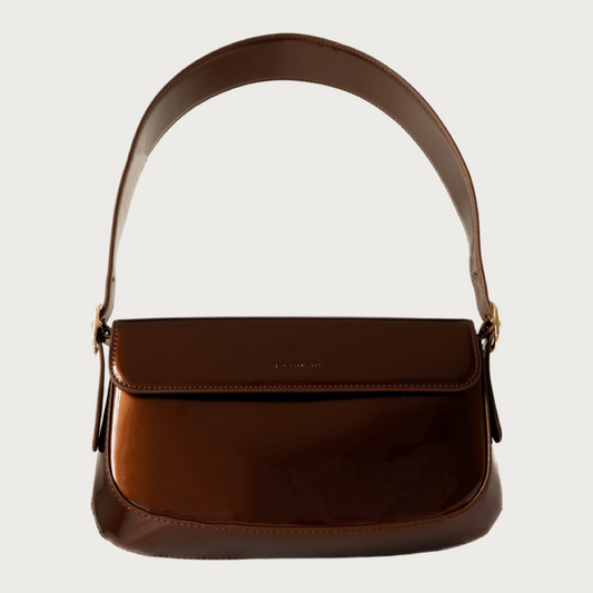 Unique baguette bag made by glossy vegan leather with asymmetrical shape. Features magnet closure and an adjustable and removable handle.