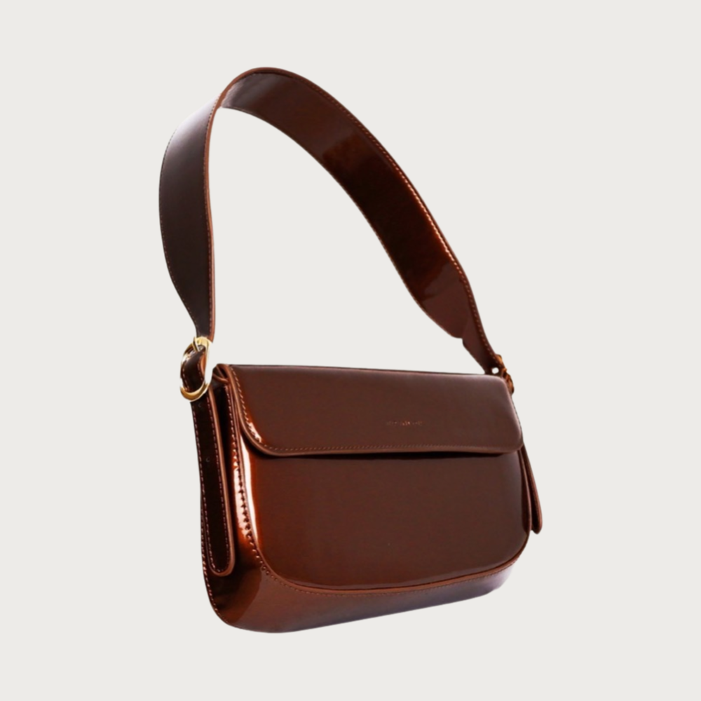 Unique baguette bag made by glossy vegan leather with asymmetrical shape. Features magnet closure and an adjustable and removable handle.